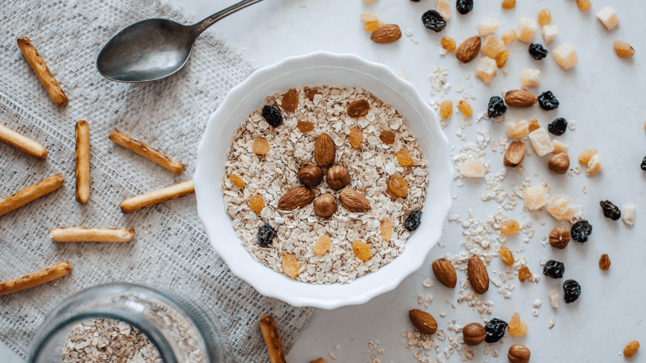 A white bowl of oats, almonds, hazelnuts, and raisins