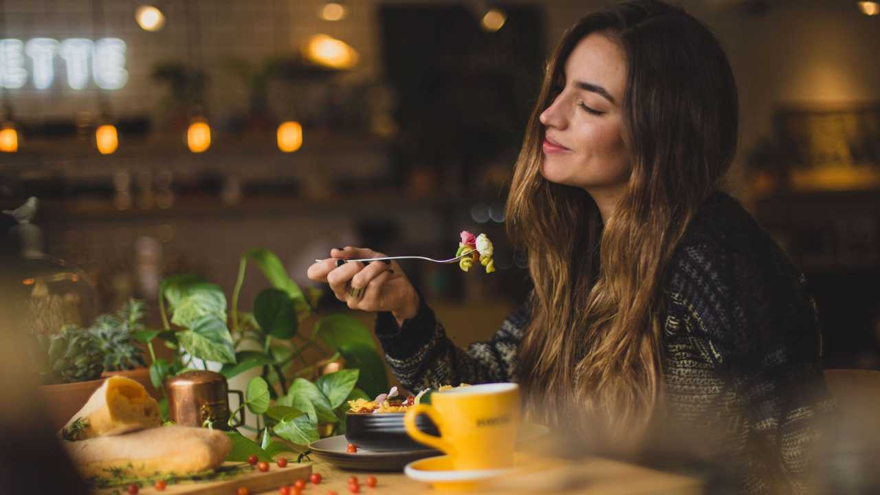 Woman in a restaurant with a smile on her face eating mindfully.